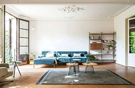 Spacious living room with plush blue sofa, wooden shelving, and decorative pendant lighting.