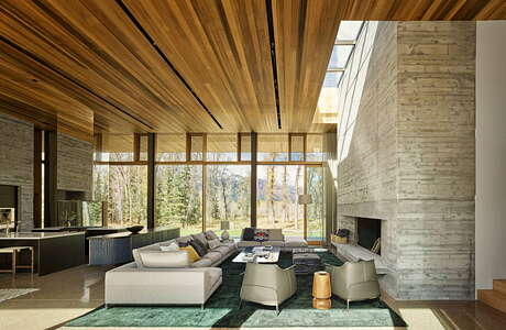 Spacious living room with wooden ceiling, stone walls, and large windows overlooking nature.