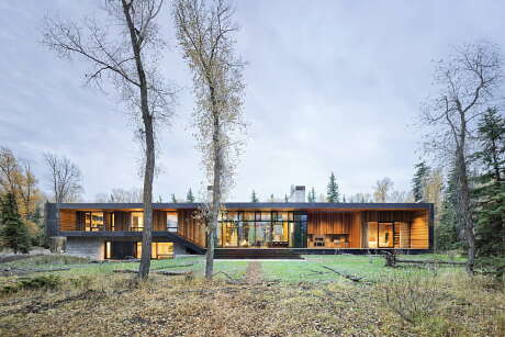 Modern two-story home with expansive glass walls, wood accents, and a natural landscape.