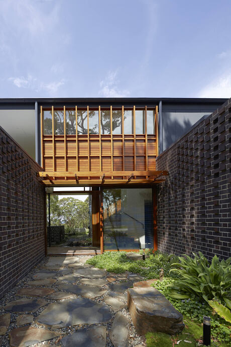 A modern architectural design featuring brick walls, wooden beams, and a paved walkway leading to the entrance.