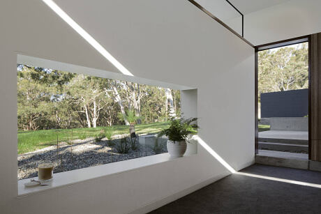 A modern, minimalist interior with large windows overlooking a lush, forested landscape.