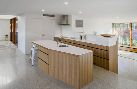 Spacious, minimalist kitchen with sleek wood cabinetry, white countertops, and modern appliances.