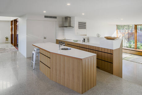 Spacious, minimalist kitchen with sleek wood cabinetry, white countertops, and modern appliances.