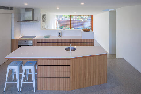 A modern kitchen with sleek white countertops, wooden cabinetry, and stainless steel appliances.