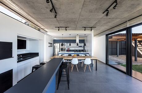 Modern open-plan kitchen and dining area with concrete ceiling, track lighting, and large windows.