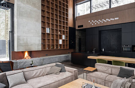 A cozy, modern living room with a fireplace, built-in wooden shelving, and sleek kitchen.