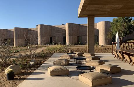 An expansive outdoor lounge area with concrete structures, cushioned seating, and desert vegetation.