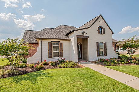 Charming single-story home with a sloped roof, decorative shutters, and nicely landscaped yard.