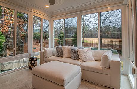 Sunlit room with large windows, beige sofa, and woodland view.