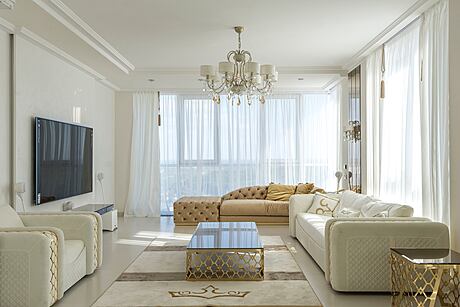 Elegant living room with white sofas, chandelier, and a flat-screen TV