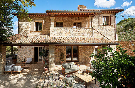 A charming stone villa with a tiled roof, surrounded by lush greenery and a cozy patio.