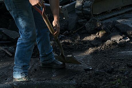 A person in work boots and jeans working with a shovel on a rocky surface.