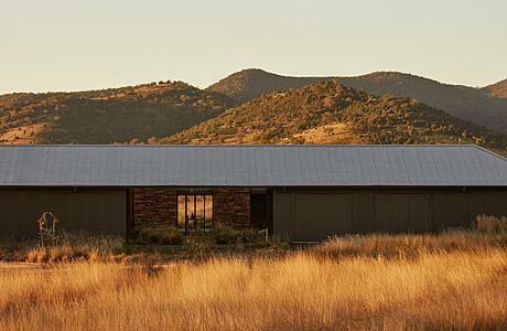 A modern ranch-style home nestled in a mountainous landscape, with a stone facade and large windows.