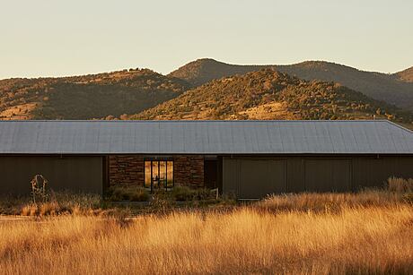 A modern ranch-style home nestled in a mountainous landscape, with a stone facade and large windows.