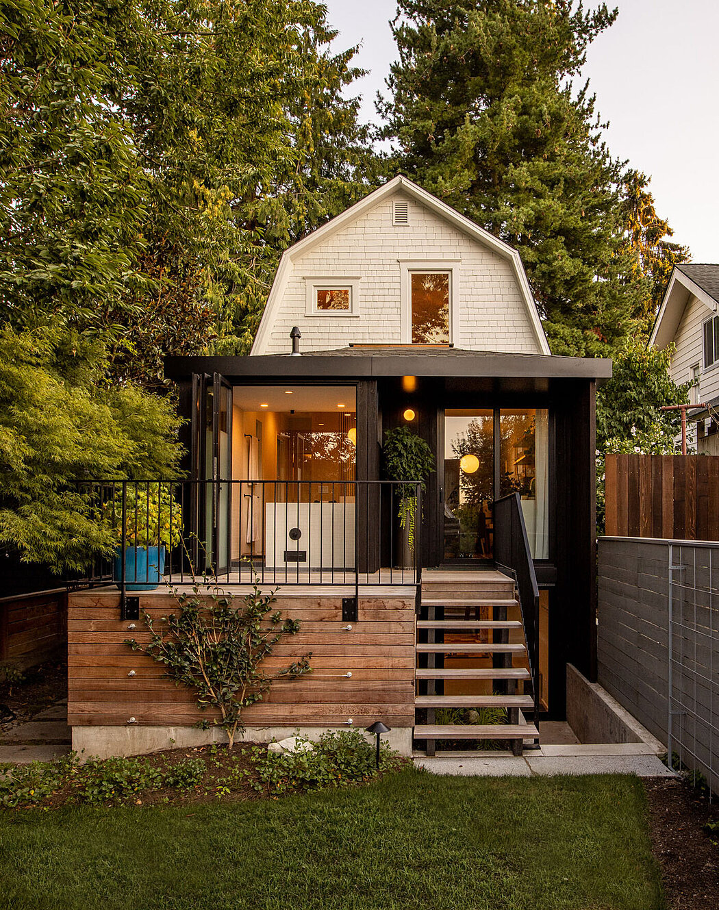 A cozy two-story home with a modern black and wooden porch at dusk.