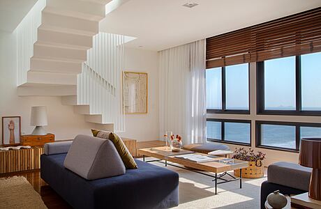 Spacious living room with sleek wooden furniture, large windows overlooking the ocean.