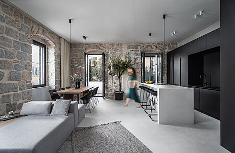 Spacious open-plan interior with stone walls, modern furnishings, and a blurred figure in motion.