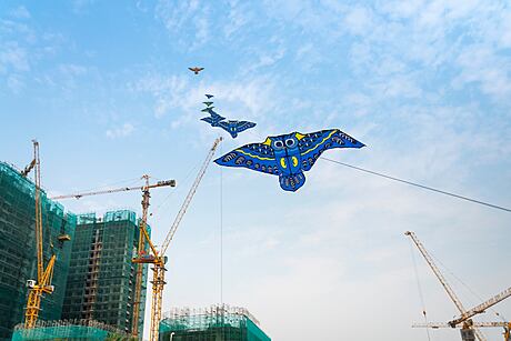 Colorful kites soaring over cranes and construction site, showcasing urban skyline.