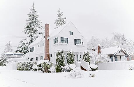 White house with snow-covered front yard and trees.