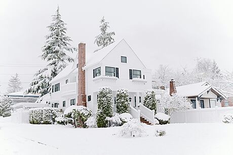 White house with snow-covered front yard and trees.