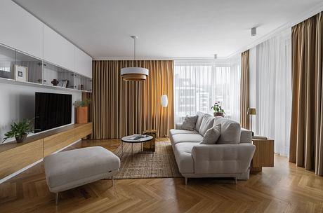 Modern living room with wooden floors, beige furniture, and large windows.