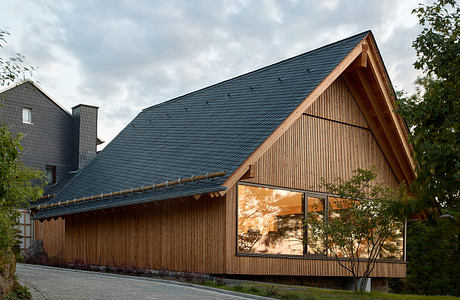 Modern wooden house with large glass windows and a sloped roof at dusk.