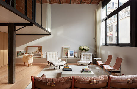 Modern living room with leather chairs, white sofas, and exposed brick walls.