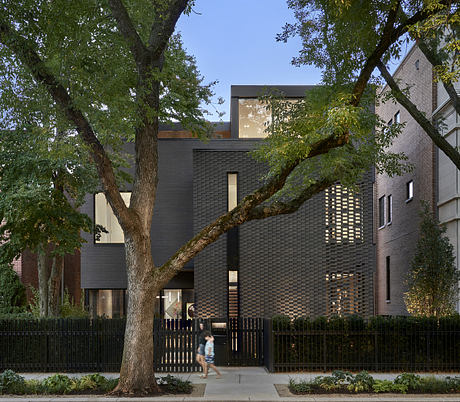 Modern two-story brick house with large trees and a fence.