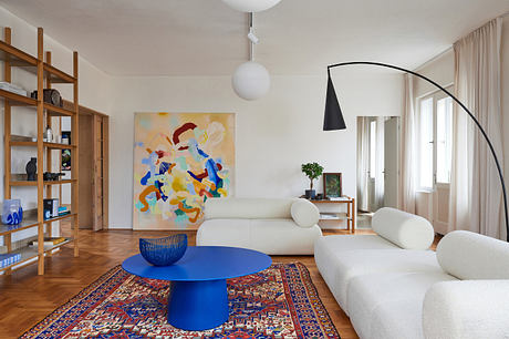 Modern living room with large abstract painting, blue table, and white sofas.