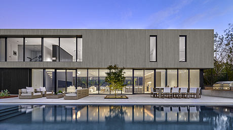 Modern two-story house with large windows and a pool at dusk.