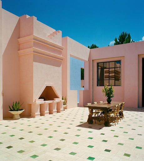 Bright courtyard with pink walls, tiled floor, rustic table, and fireplace.