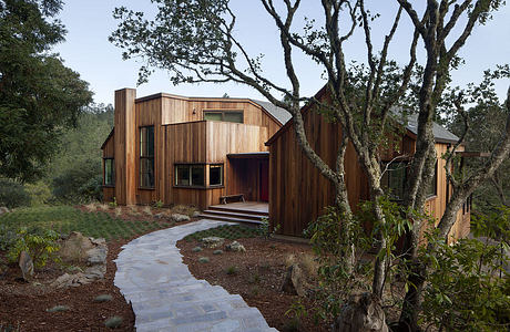 Modern wooden house with angular design amidst forest setting.