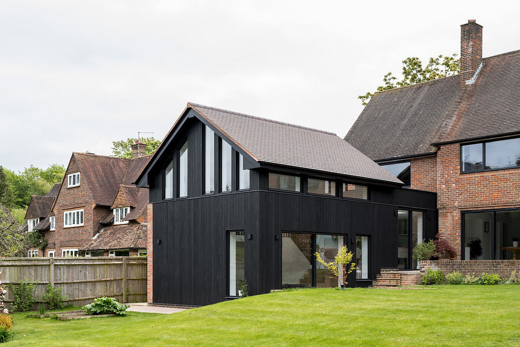 Modern black extension on a traditional brick house with a green lawn.