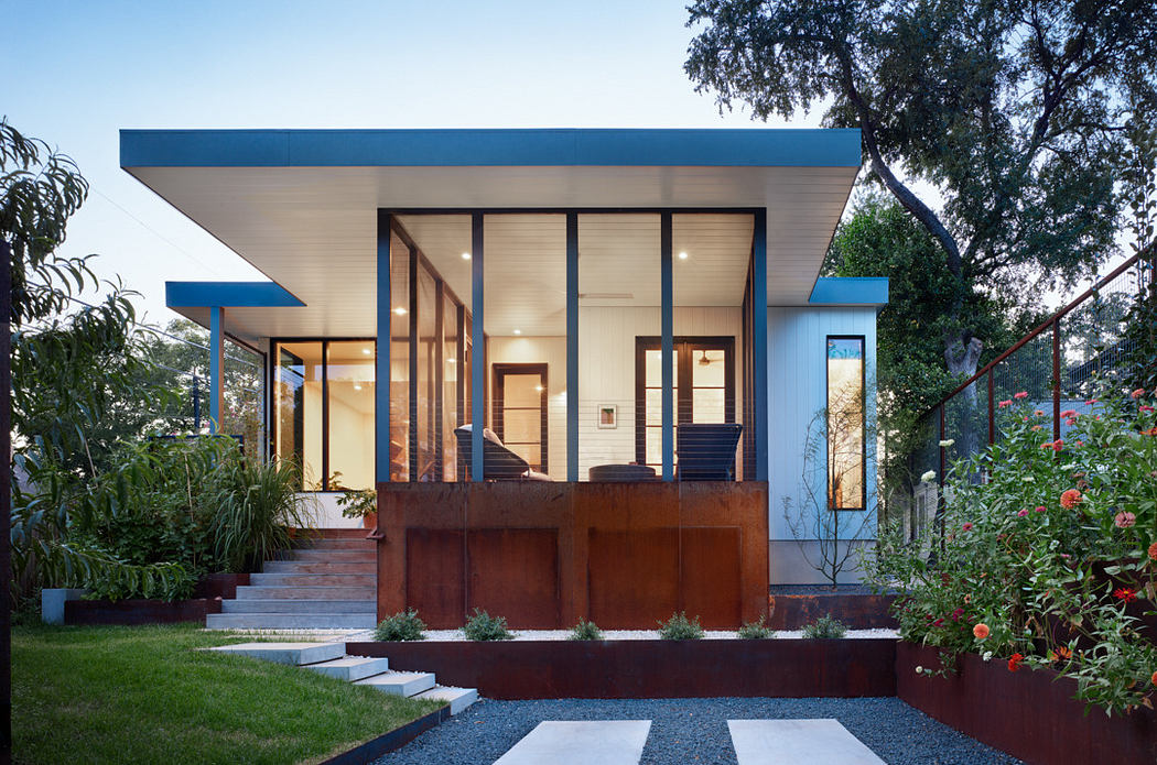 Modern house exterior at dusk with illuminated windows, blue trim, and landscaped garden