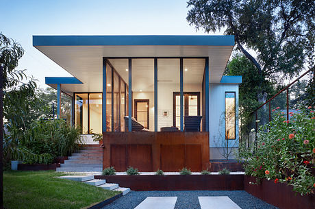 Modern house exterior at dusk with illuminated windows, blue trim, and landscaped garden