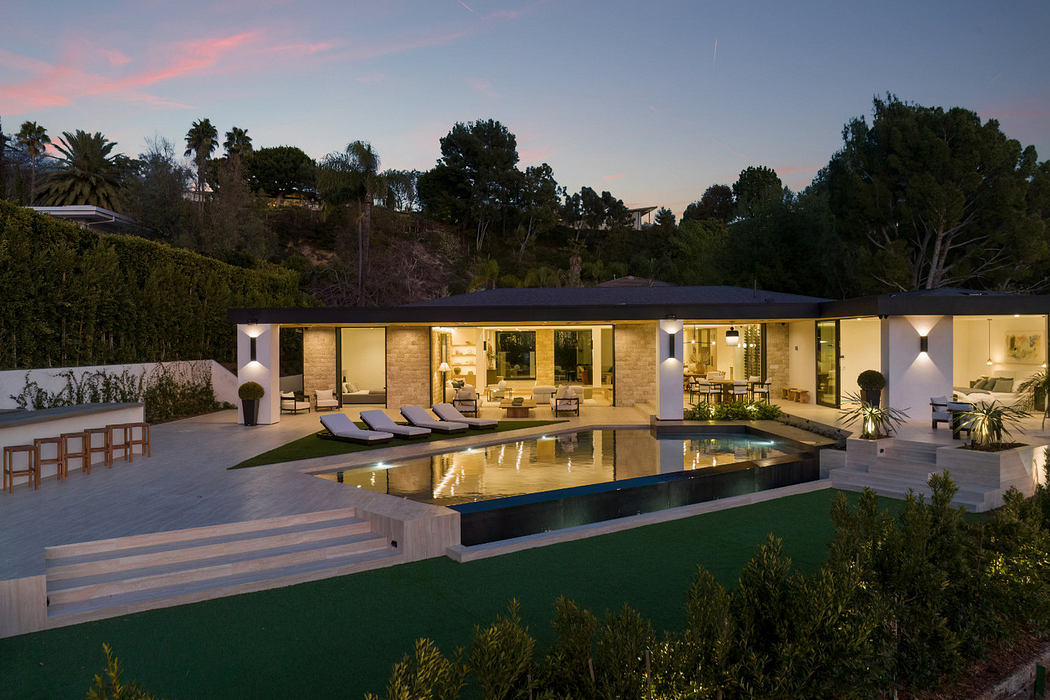Modern house with large windows, a pool, and outdoor lighting at twilight.