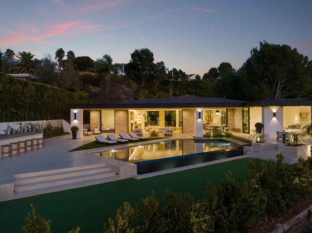 Modern house with large windows, a pool, and outdoor lighting at twilight.