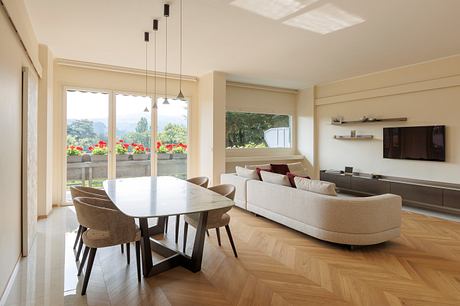 Modern living room with a dining area, sofa, and large windows.