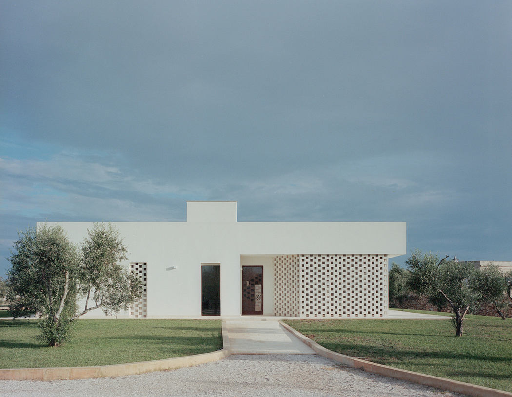 Modern white house with perforated wall design and olive trees.