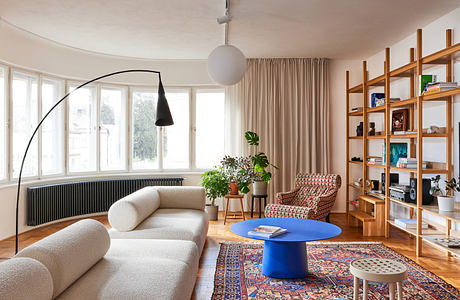 Modern living room with curved sofa, wooden bookshelf, and large window.