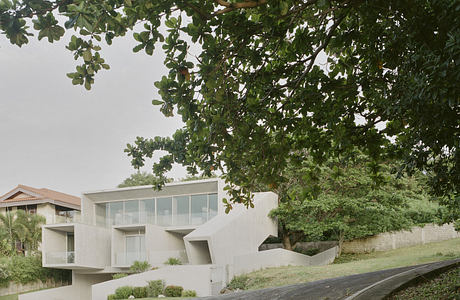 Modern concrete house with large windows, framed by green foliage.