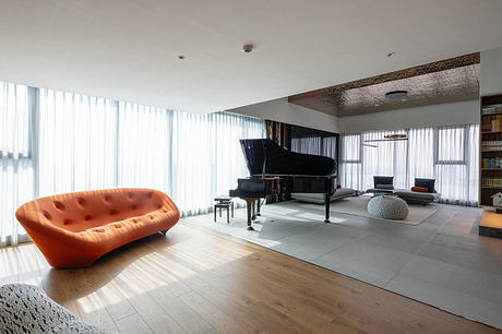 Modern living room with large windows, an orange sofa, and a grand piano.