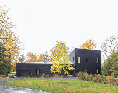 Modern black-clad house with asymmetrical design surrounded by autumn trees.