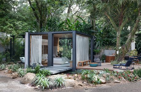 Modern glass-walled cabin surrounded by lush greenery.