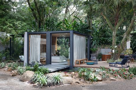 Modern glass-walled cabin surrounded by lush greenery.