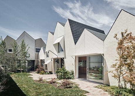 Modern residential complex with peaked roofs and white facades, surrounded by greenery.