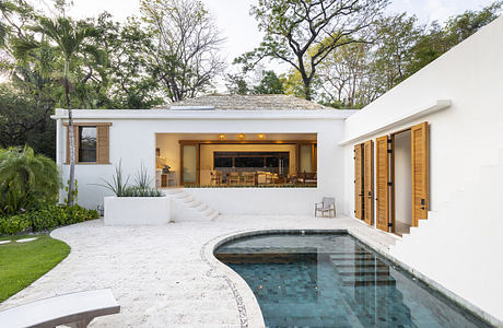 Modern white villa with open living space and curved pool surrounded by greenery.