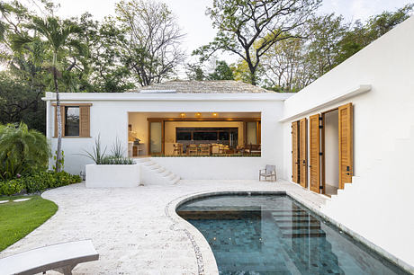 Modern white villa with open living space and curved pool surrounded by greenery.