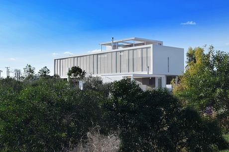 Modern white house with flat roof amidst greenery.