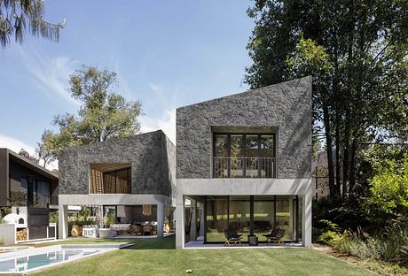 Modern two-story house with stone facade, large windows, pool, and lawn.